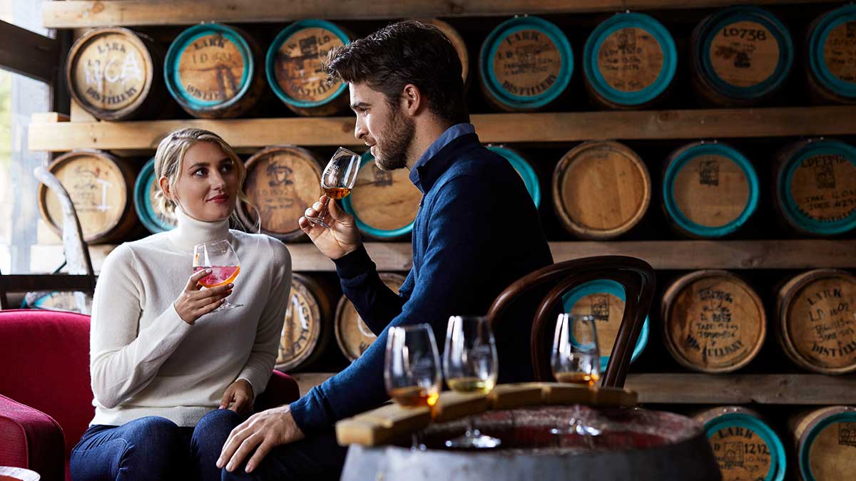 two people drinking wine next to a wine barrell