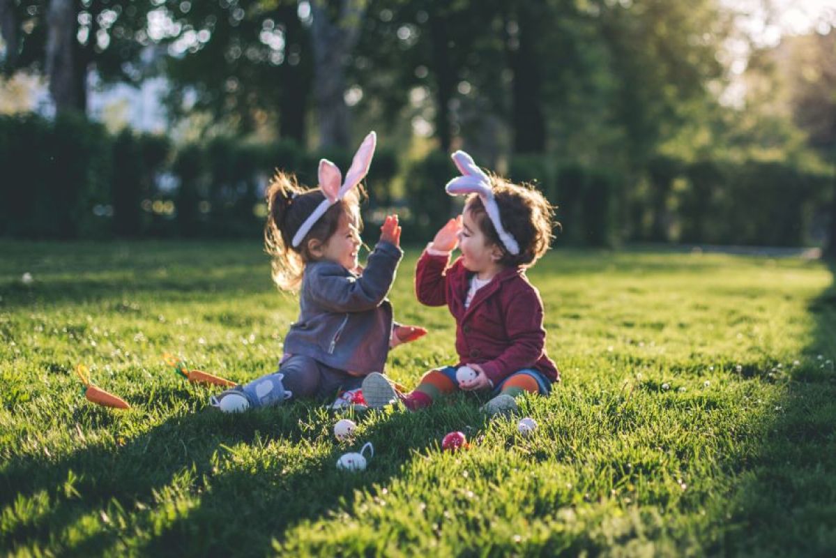 two young children dressed in bunny ears playing in the grass with Easter eggs