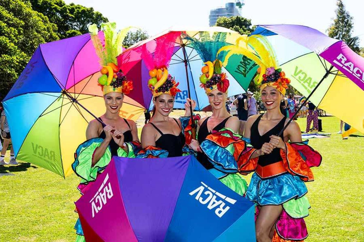 four women dressed up with rainbow umbrellas sporting the RACV logo