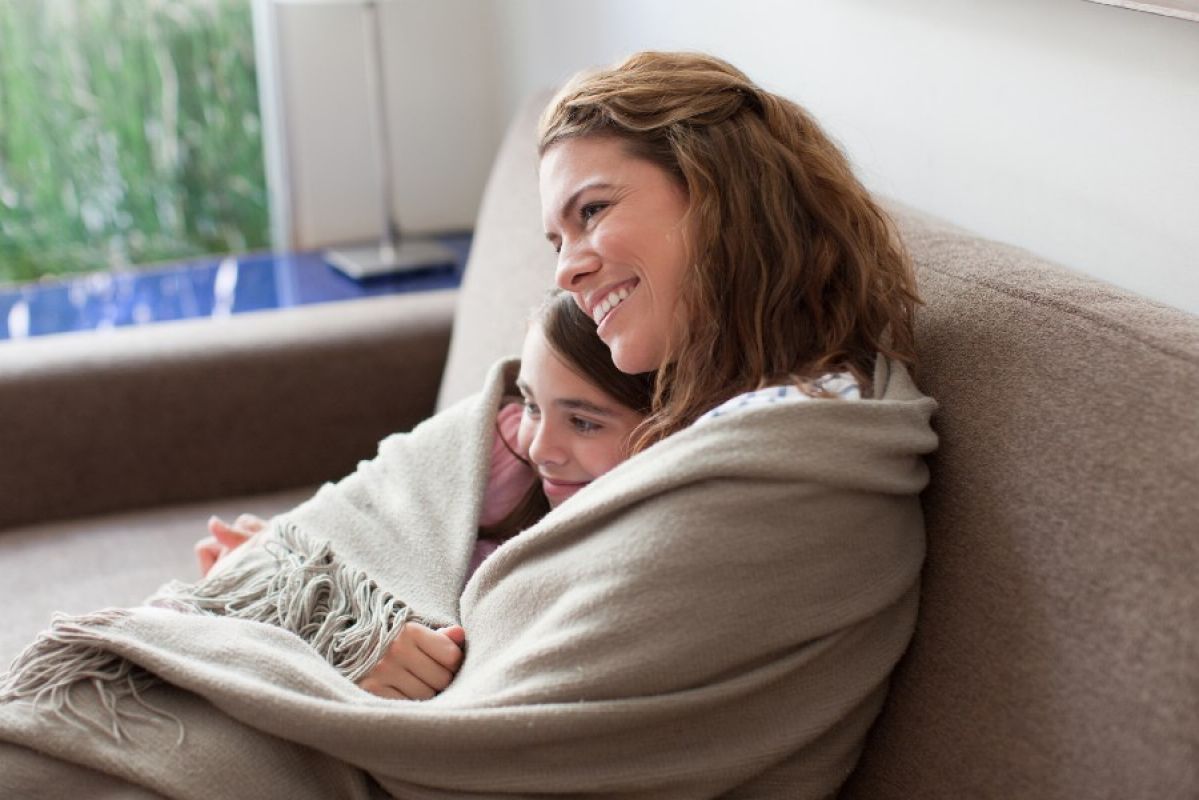 mother and daughter wrapped in a blanket on the couch