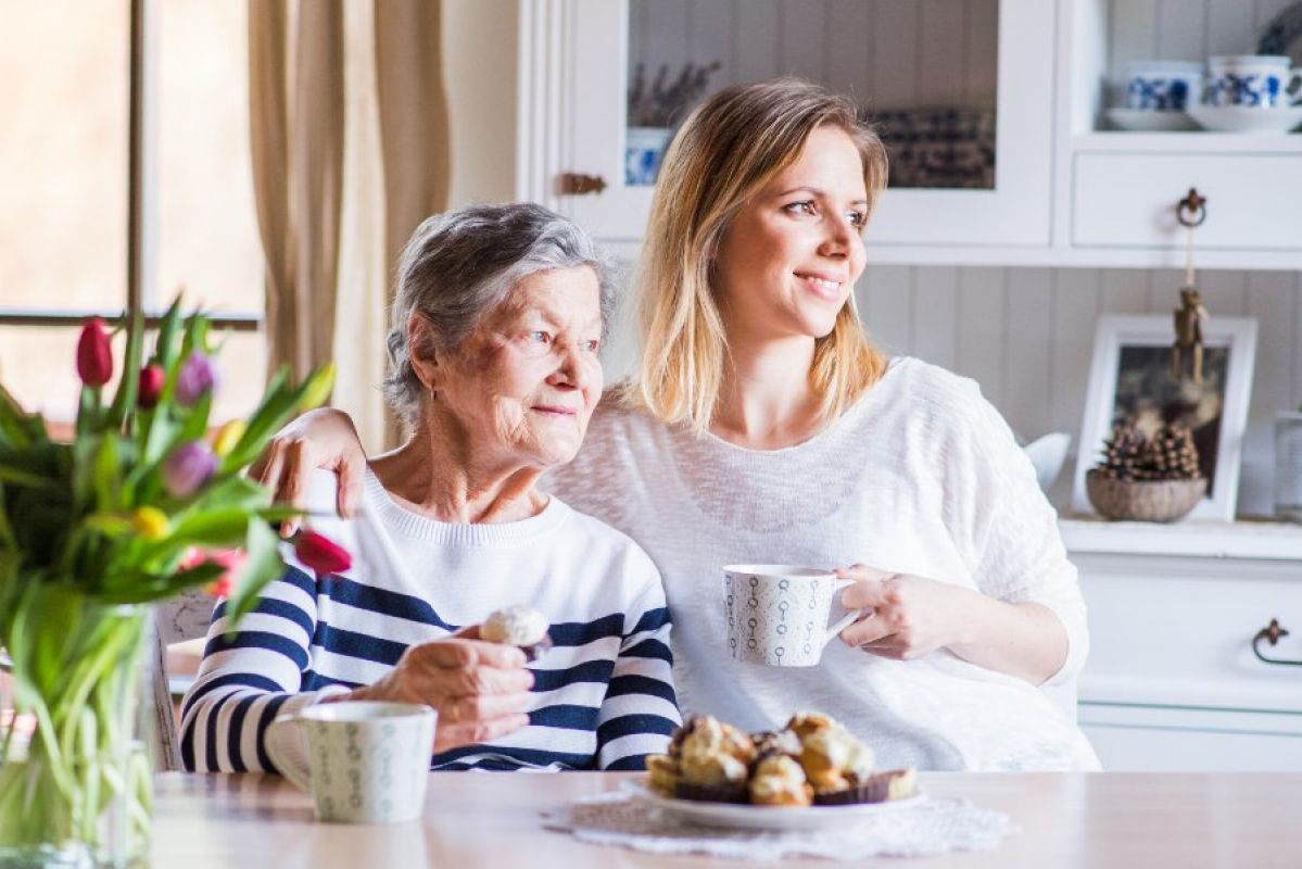 adult woman and her elderly mother sitting drinking tea together