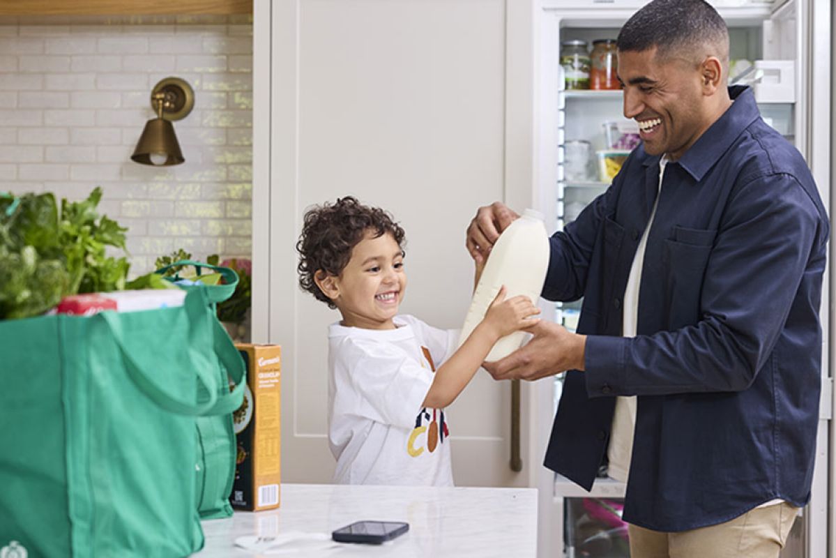 A man and child gleefully putting away a bag of groceries