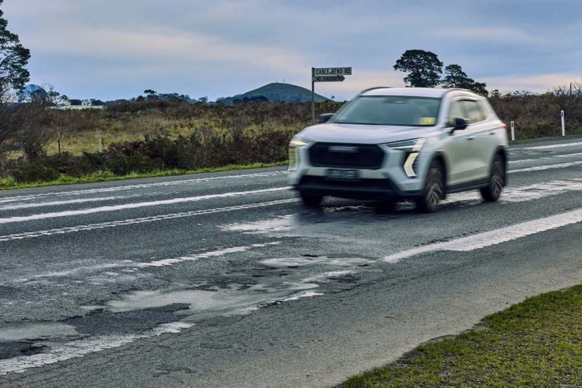 A white SUV driving along a rough section of road between Colac and Camperdown on the Princes Highway
