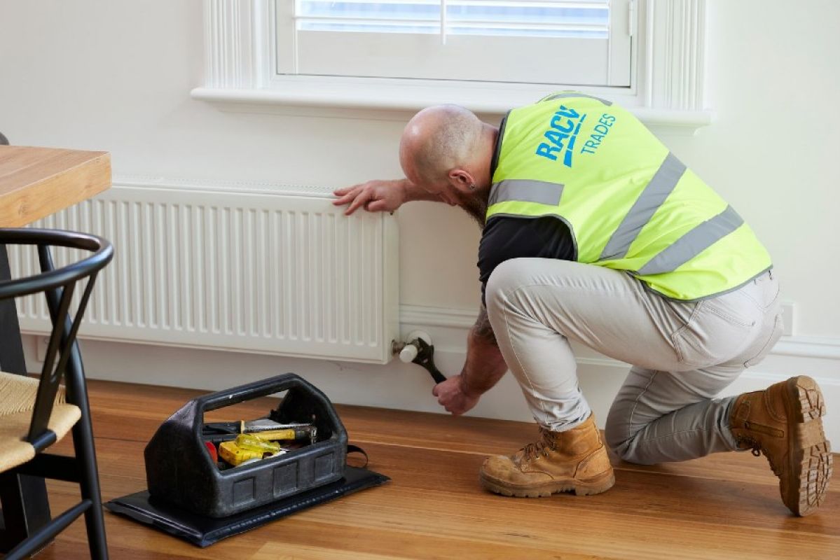 A technician wearing an RACV-branded safety vest adjusts a hydronic heater