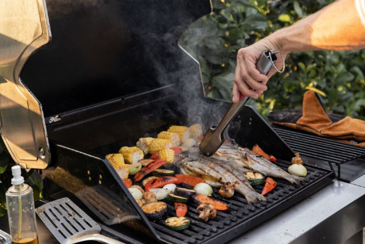 A person cooking an assortment of meat, fish and vegetables on a gas barbecue