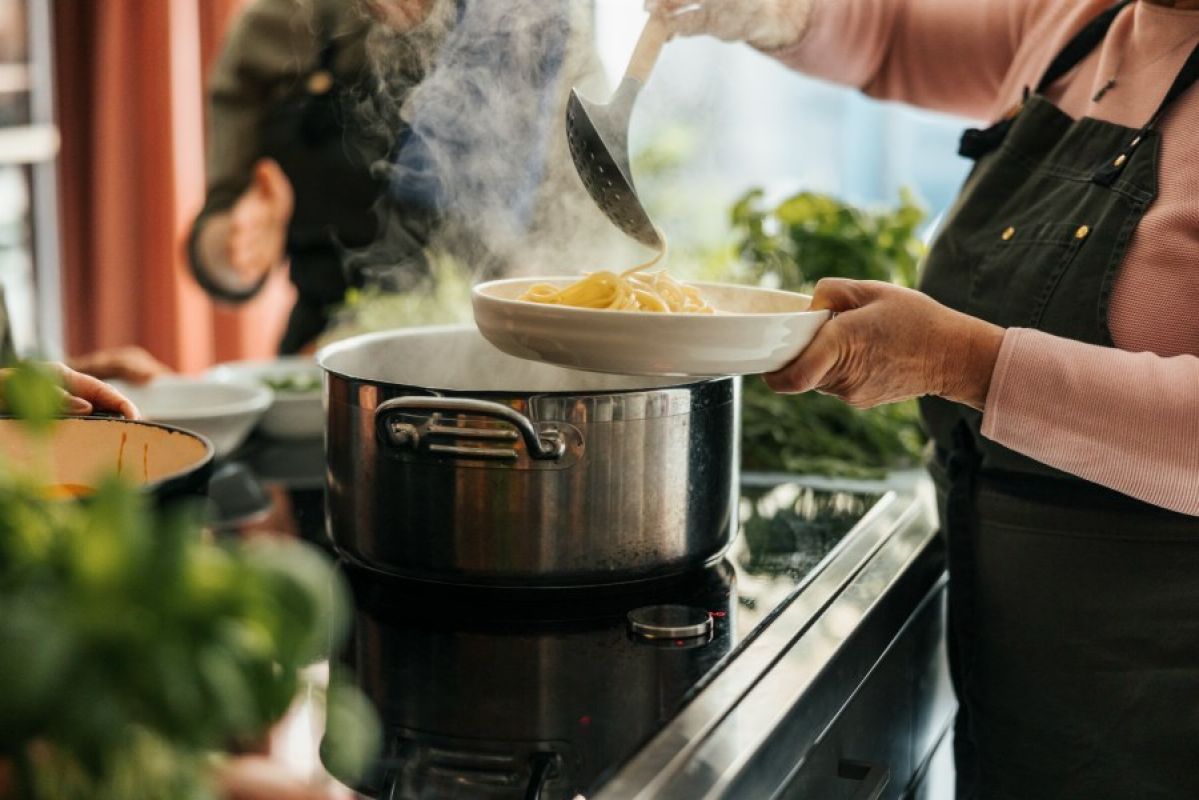 woman lading spaghetti out of pot on induction cooktop
