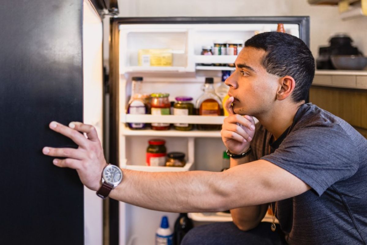 young man looking into his fridge