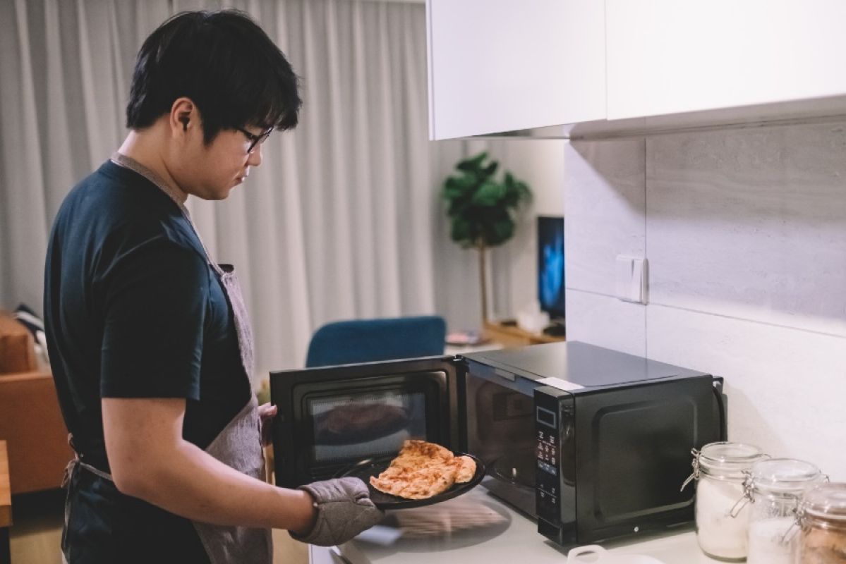 young man using oven gloves to take a plate of food out of a microwave