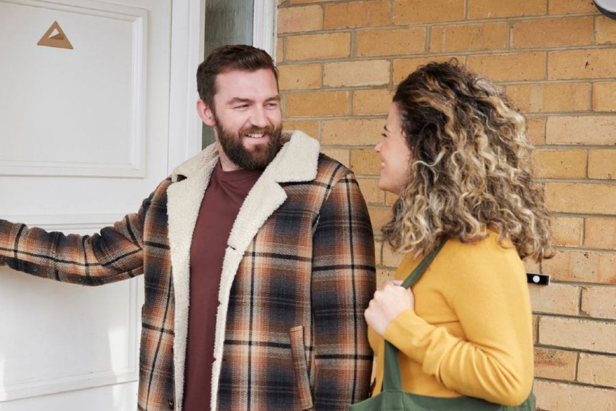 A man and woman happily about to enter a house through the front door