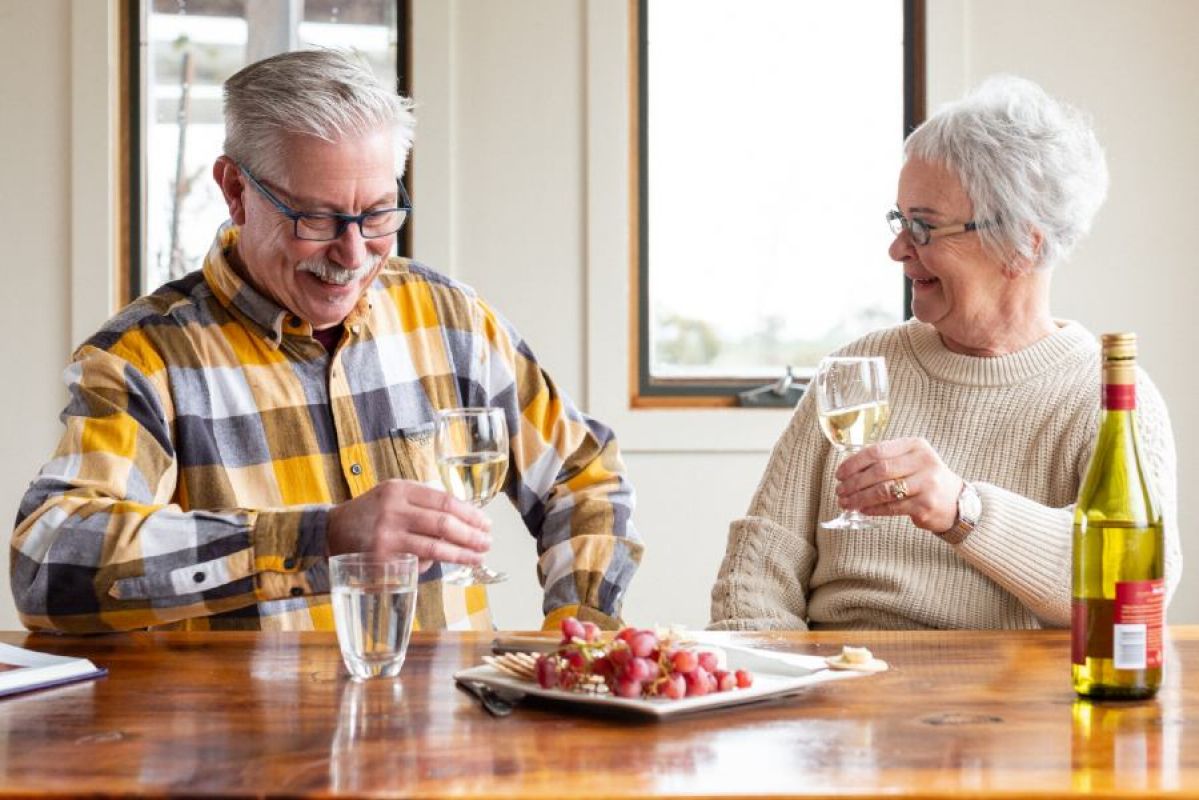 A senior man and woman smiling as they enjoy wine and a fruit platter at home