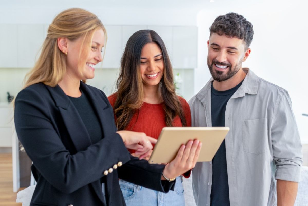 A couple looking happily at a digital tablet held by a sales person in a display home for off-the-plan homes