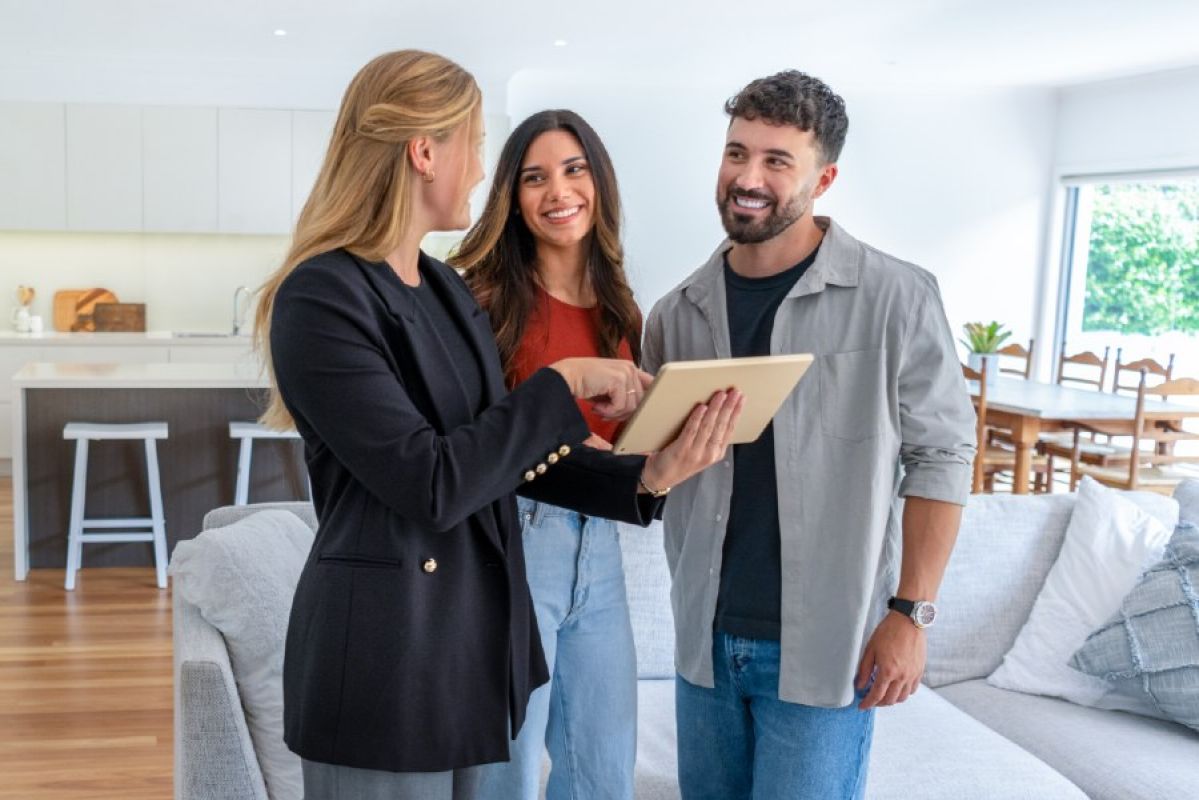 real estate agent showing two homeowners something on a tablet in their home