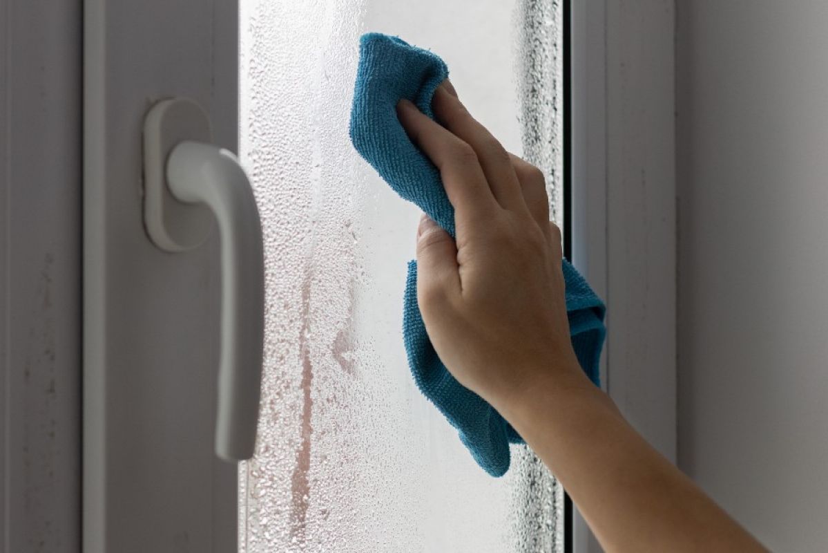 A hand using a blue cloth to clean a window covered in condensation