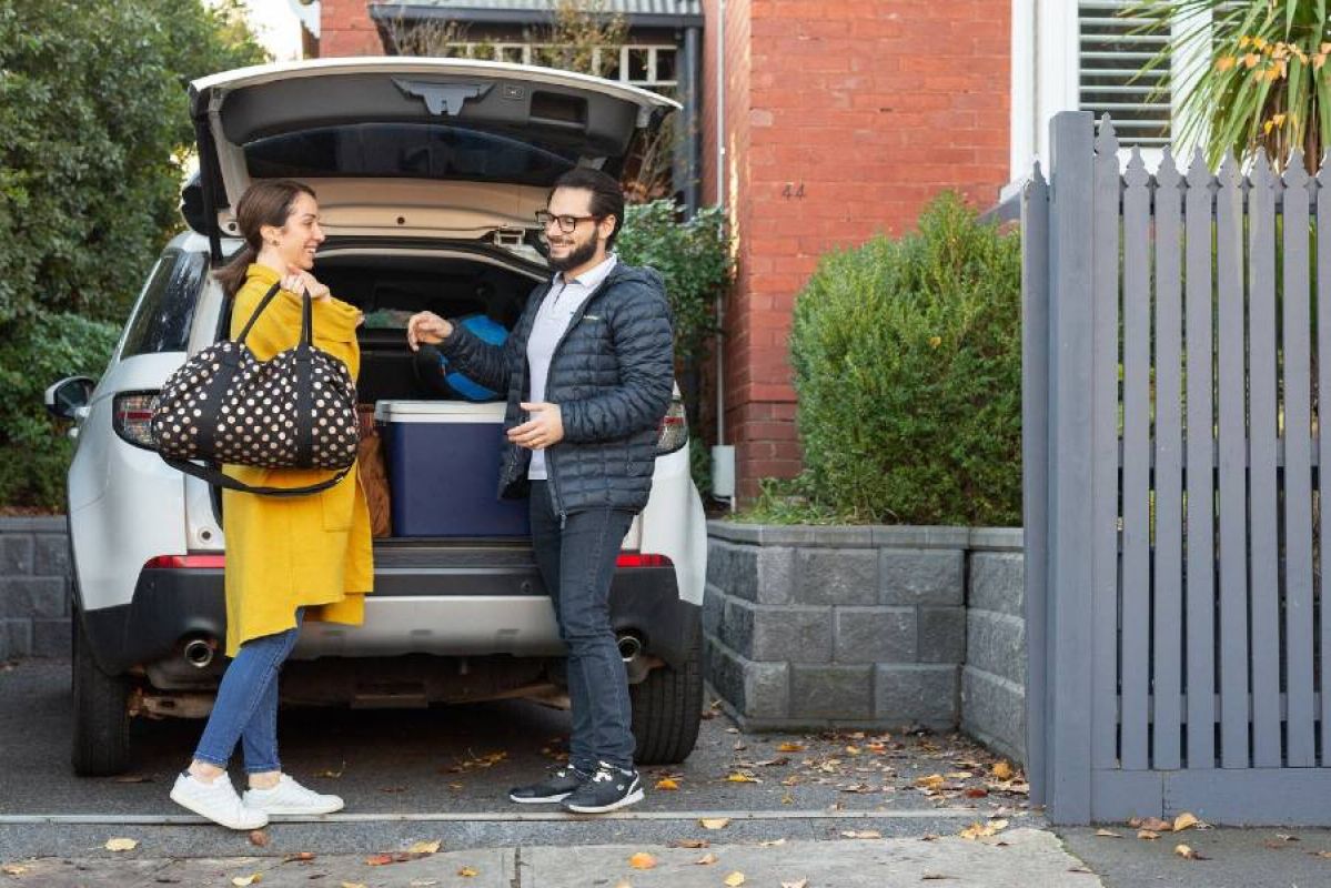 A woman and man happily taking luggage out of a SUV parked in a suburban driveway