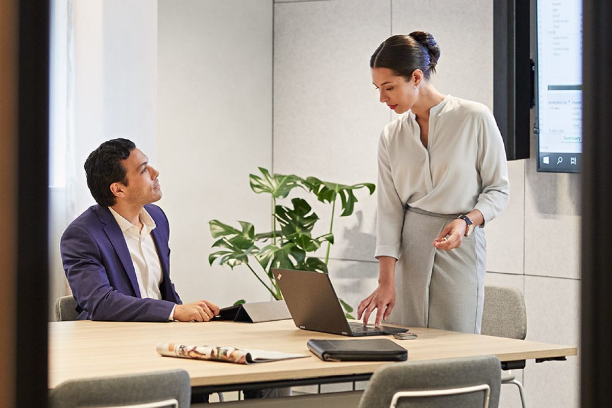 Professional woman presenting in business centre with laptop to male client seated at table