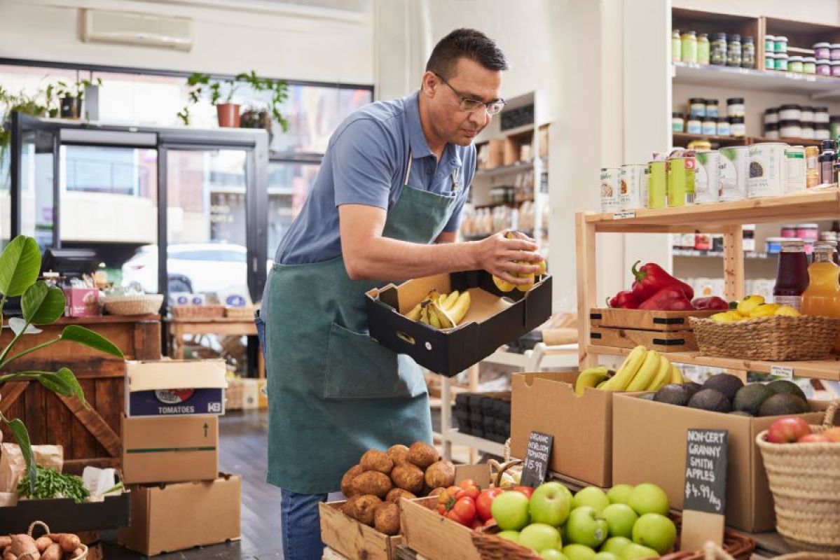man in apron stocking grocer shelves with fruit