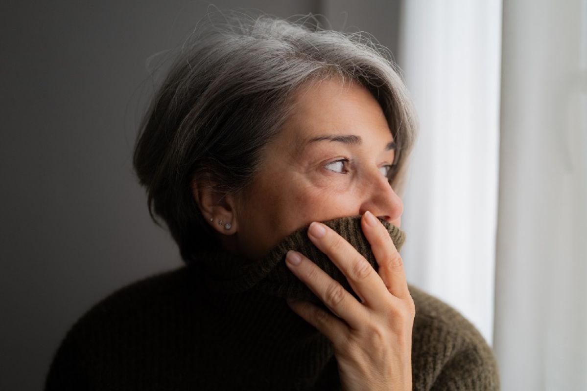 middle-aged woman pulling her sweater over her mouth and looking concerned inside her house