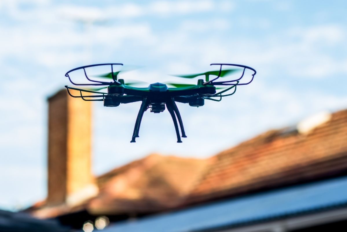 drone in flight with suburban home roof in background