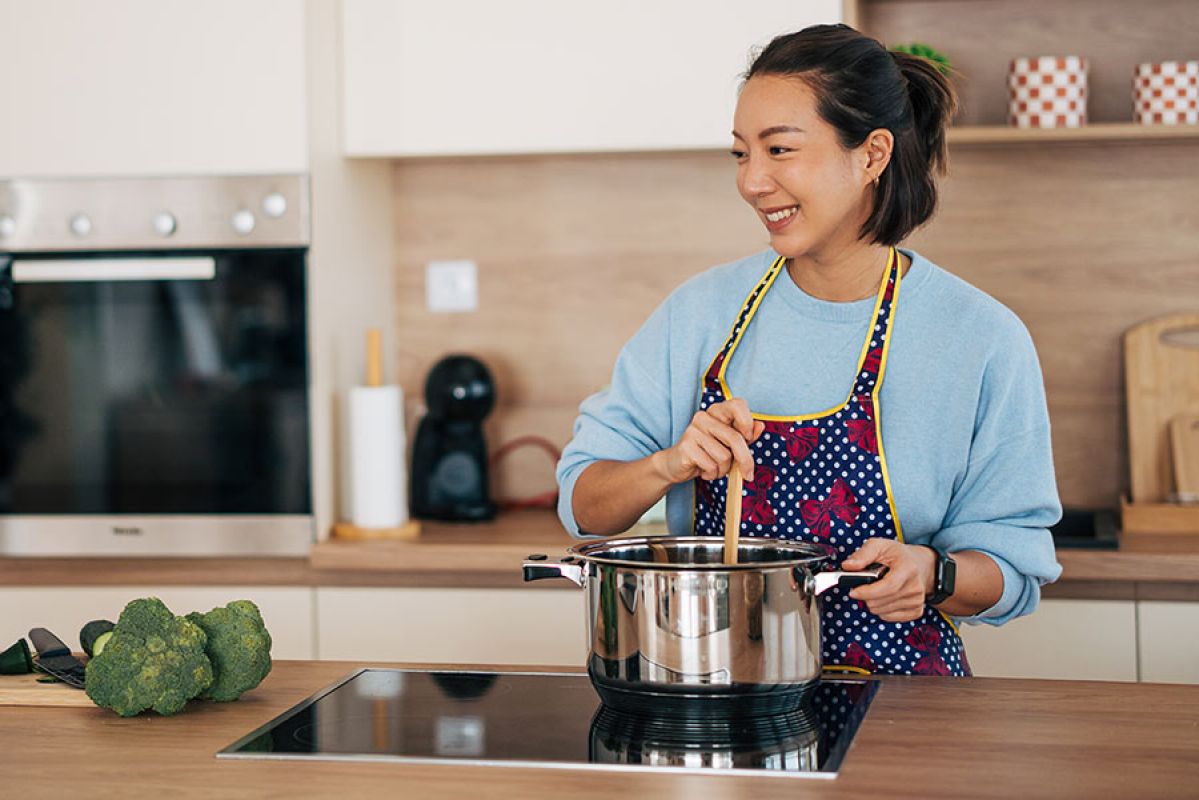 A woman smiles as she stirs a pot on an induction cooktop.