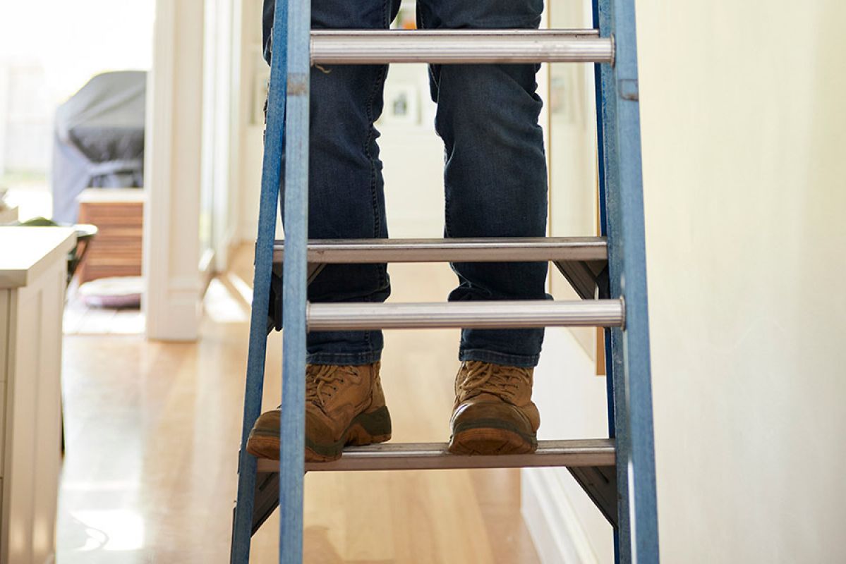 Person in jeans with brown boots on a stepladder in hallway with image showing feet on first step