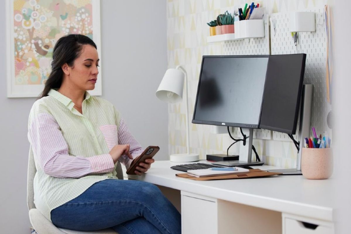 A woman on her phone in front of a desktop computer at home