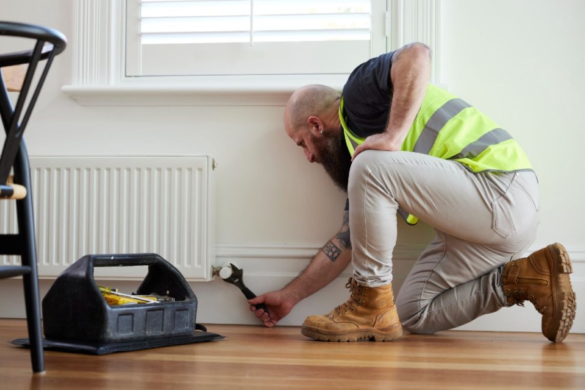 A tradesperson in a hi vis vest adjusts a hydronic heater with a wrench