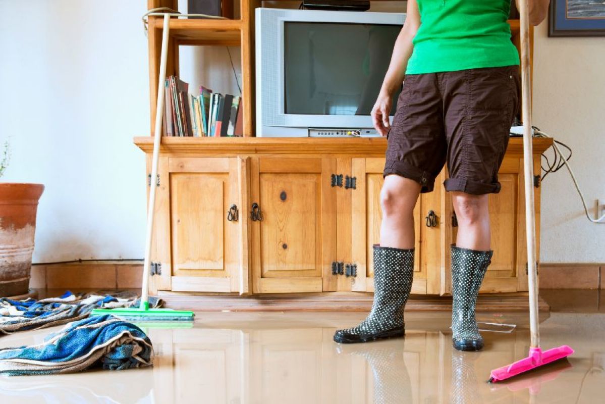 woman in gumboots cleaning up flood damage in her home