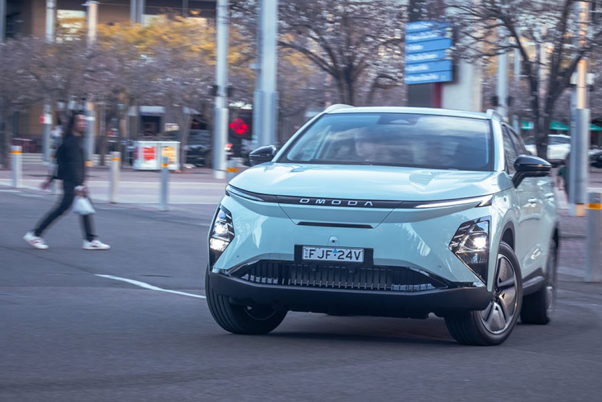 Chery Omoda E5 electric car turning corner on city street with pedestrian crossing road behind