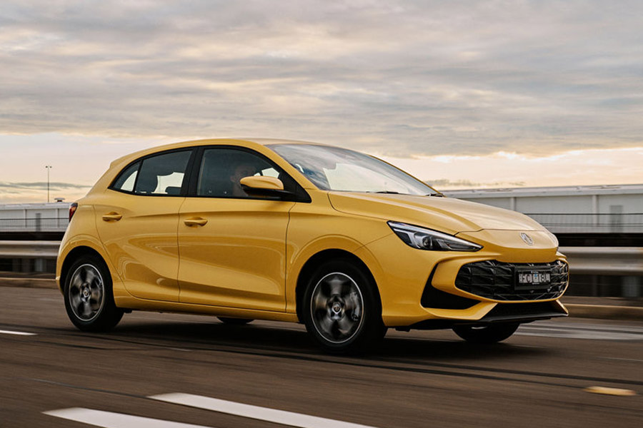 Yellow MG3 hybrid hatchback driving on multi-lane overpass with bright sky in background
