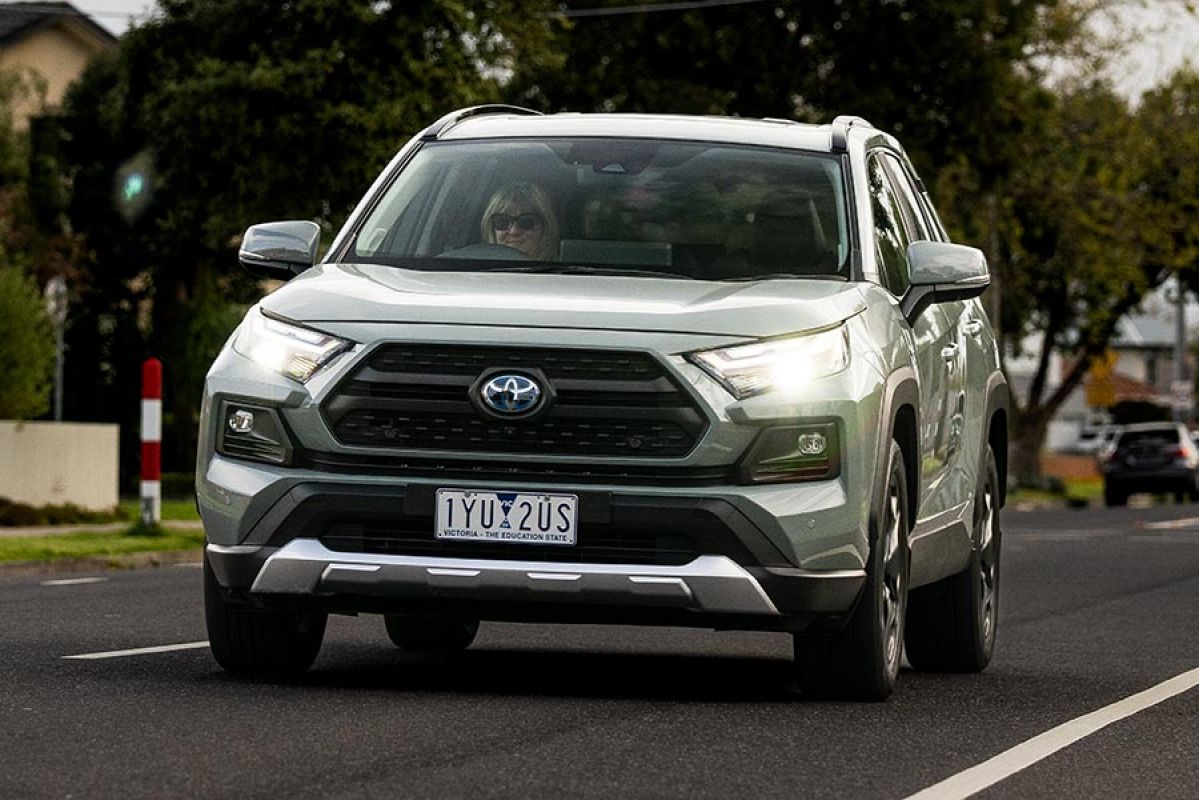 Woman driving light green Toyota RAV4 Edge Hybrid medium SUV on suburban road past children's crossing