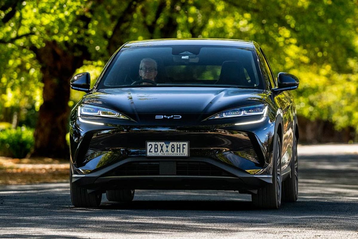 Black BYD Sealion 7 electric family SUV driving on light-filled leafy suburban street in Victoria.