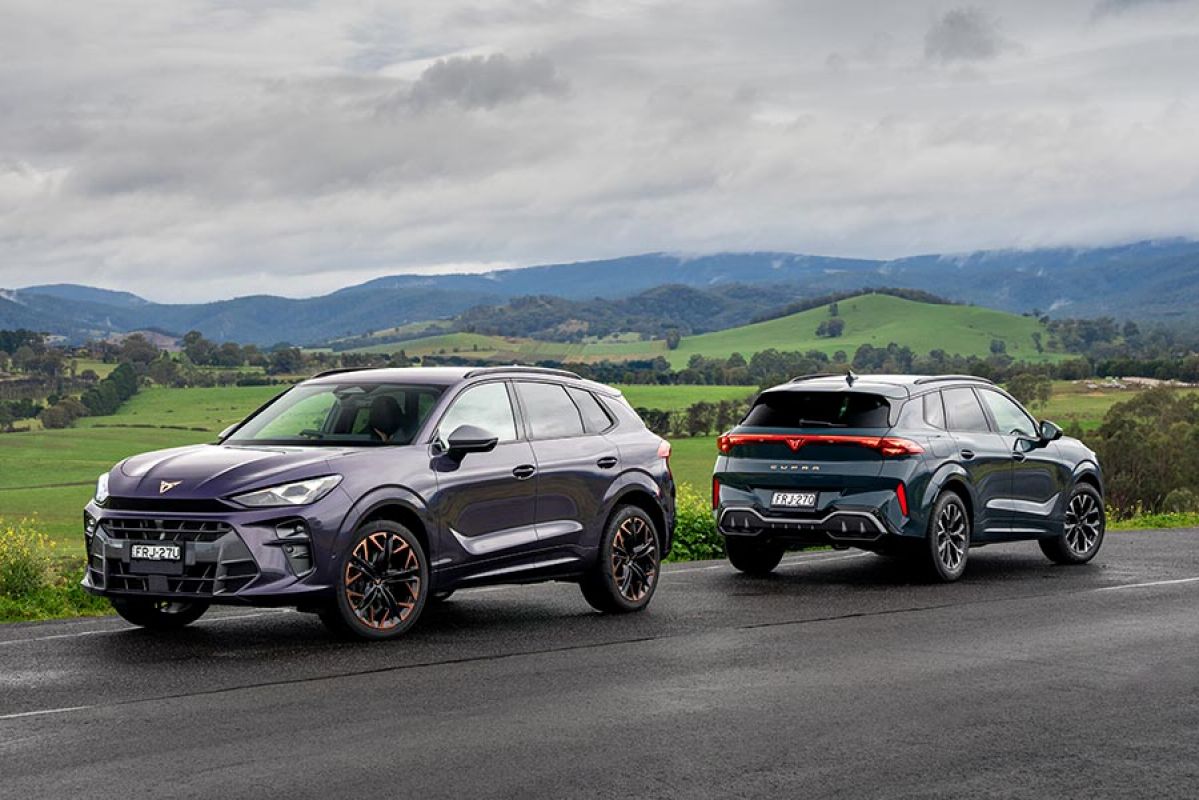 Purple Cupra Terramar VZ and blue Terramar S medium SUVs on country road with green rolling hills behind.