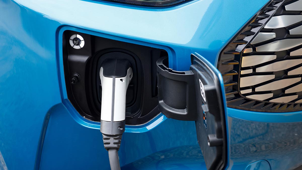 EV charging flap open and white plug attached in blue Ford E-Transit van.