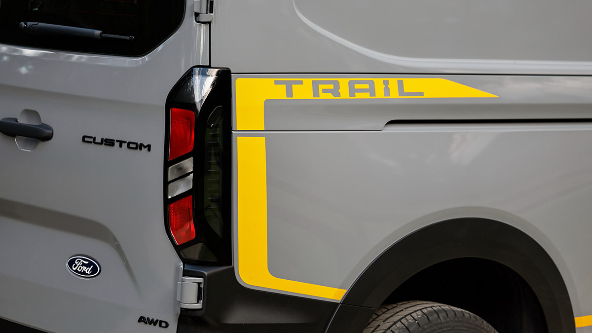 Bright yellow sticker stripe with Trail badge on rear quarter of Ford Transit Custom Trail van.
