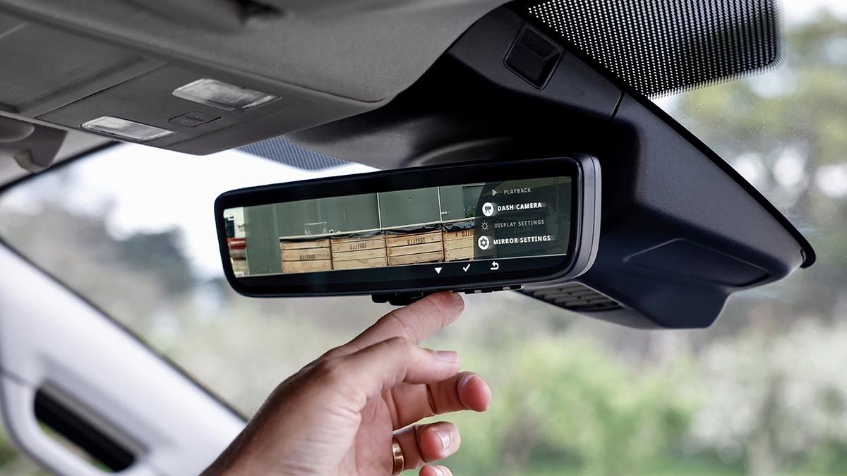 Hand touching buttons on digital rearview mirror on windscreen of Ford Transit van.