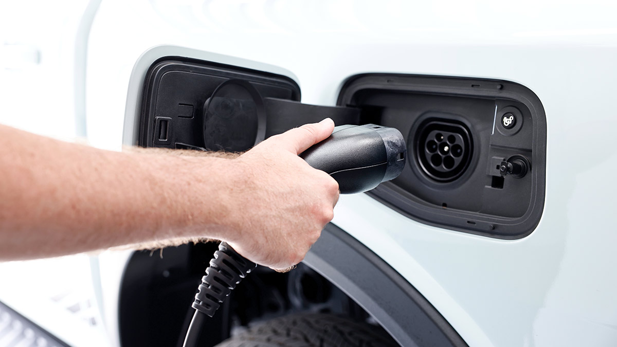 Man plugging battery charging cable into socket behind flap of Ford Ranger PHEV