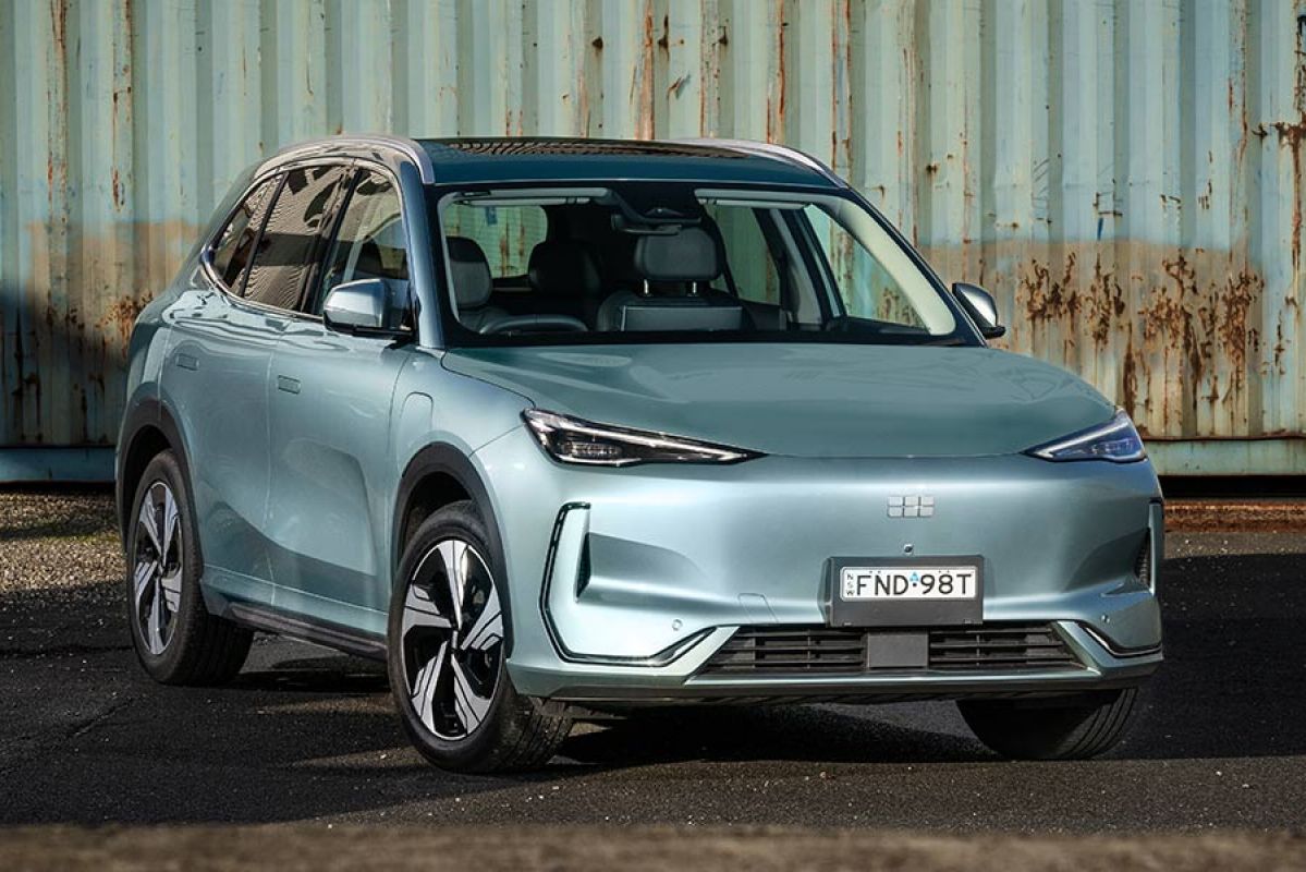 Grey-blue Geely EX5 Inspire medium SUV in front of rusty shipping container