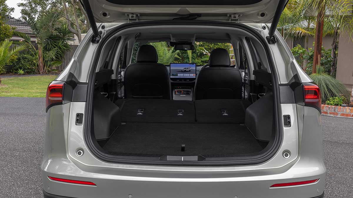 Pearl-coloured GWM Haval H6 plug-in hybrid SUV parked in suburban driveway with tailgate up and rear seats folded.