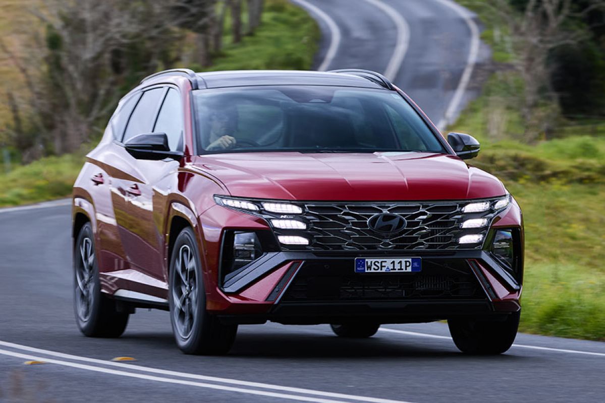 Red Hyundai Tucson Premium N Line Hybrid SUV taking a corner on a country road.