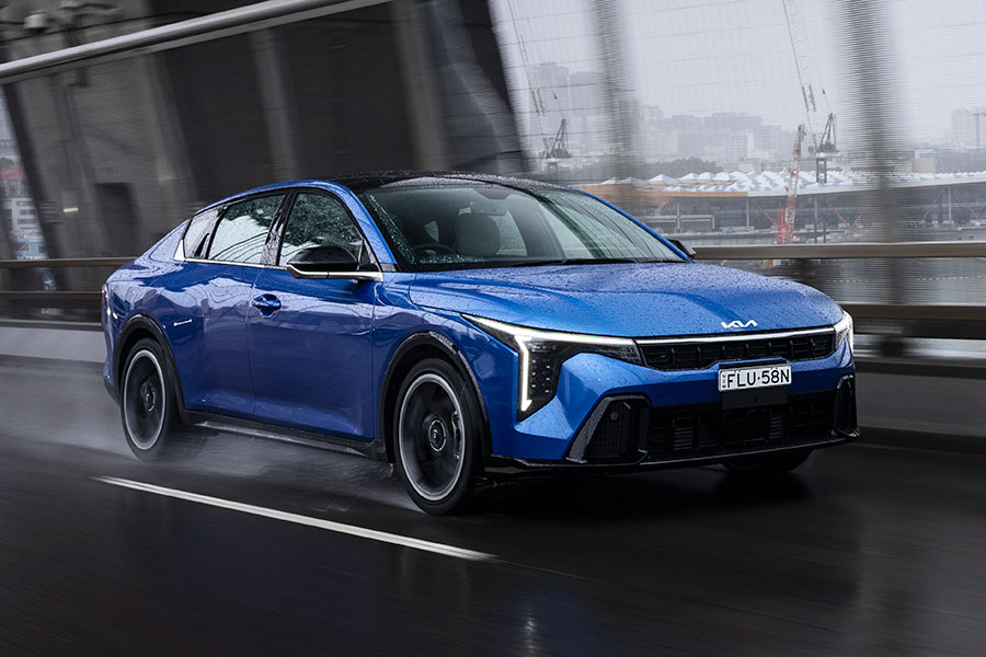 Blue Kia K4 sedan driving across large bridge in wet weather