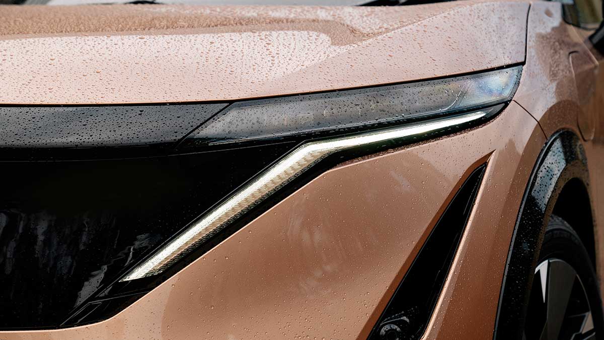 Boomerang-shaped daytime running light and thin headlight on copper-coloured Nissan Ariya Evolve electric SUV.