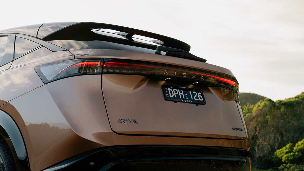 Rear view of copper-coloured Nissan Ariya electric SUV parked on side of coastal road.