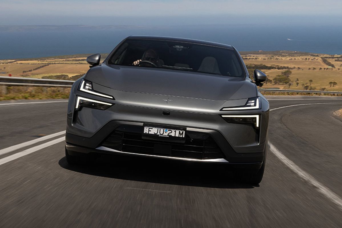 Grey metallic Polestar 4 SUV driving uphill on rural highway with ocean in background