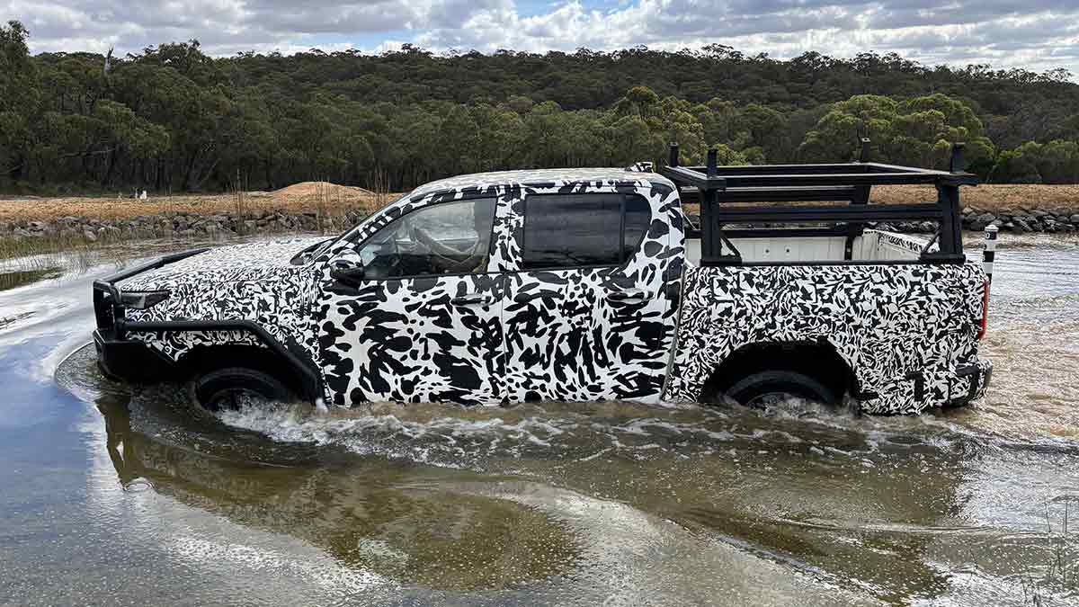 Camouflaged Toyota HiLux going through water crossing with Australian bush in background.
