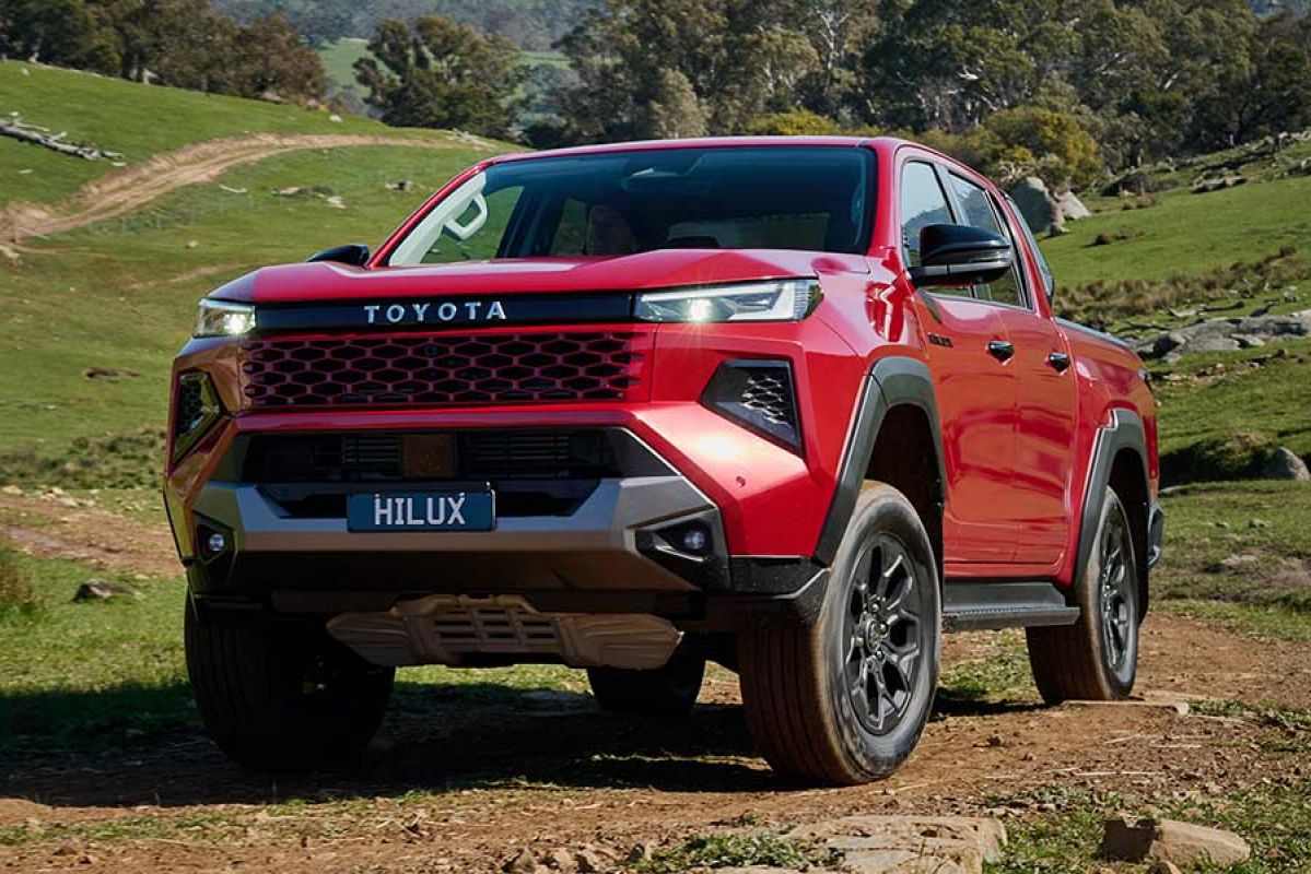 Red Toyota HiLux Rogue ute on hilly, rocky off-road trail with bush behind.