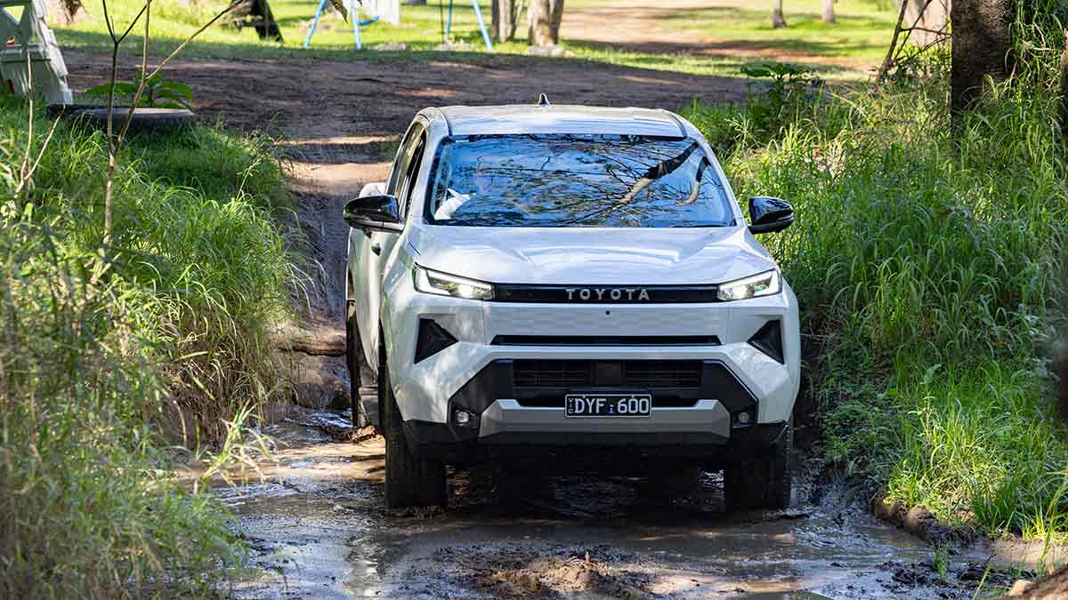 White Toyota HiLux SR5 EV crossing shallow muddy creek at off-roading adventure park in Queensland.