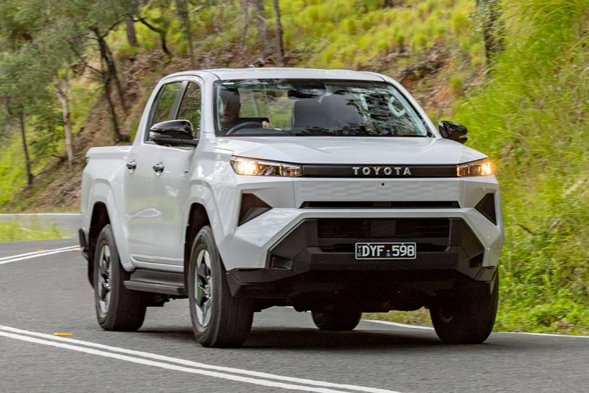 White Toyota HiLux electric dual-cab ute driving on winding high-banked country bitumen road.