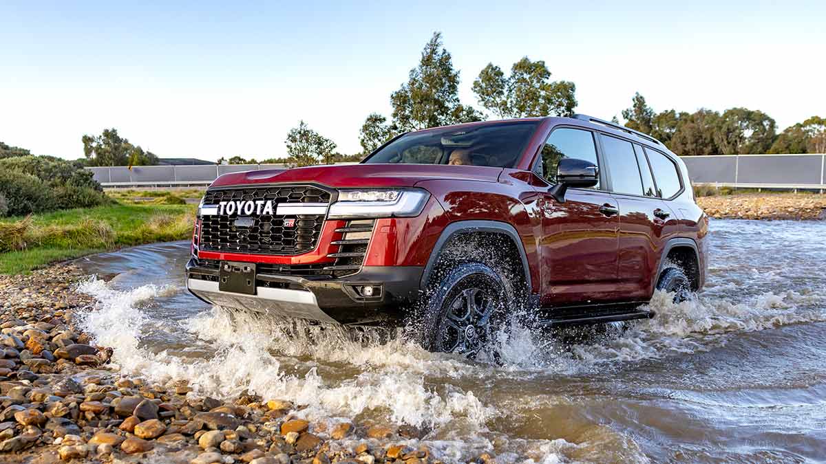 Red Toyota LandCruiser Hybrid driving through water crossing at proving ground in Altona.
