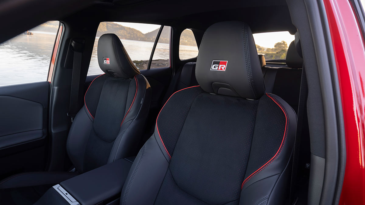 Front seats in Toyota RAV4 GR Sport with dark synthetic leather trim, suede inserts, red stitching and red GR logo in headrest.