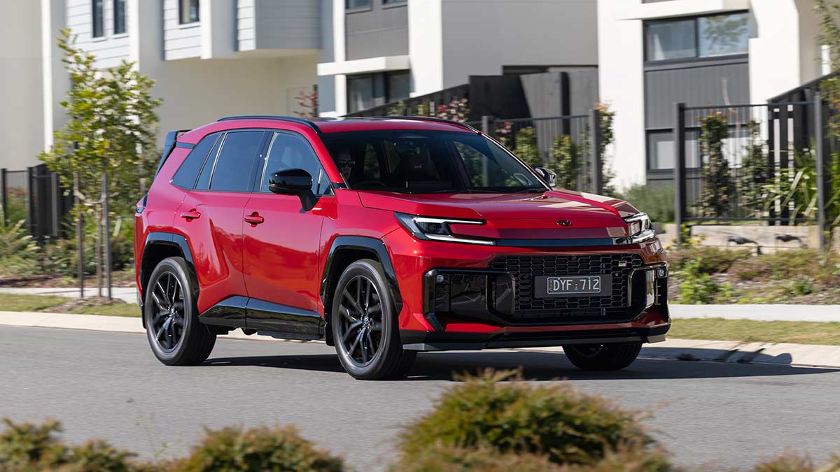 Red Toyota RAV4 GR Sport PHEV on suburban street lined with modern white townhouses.